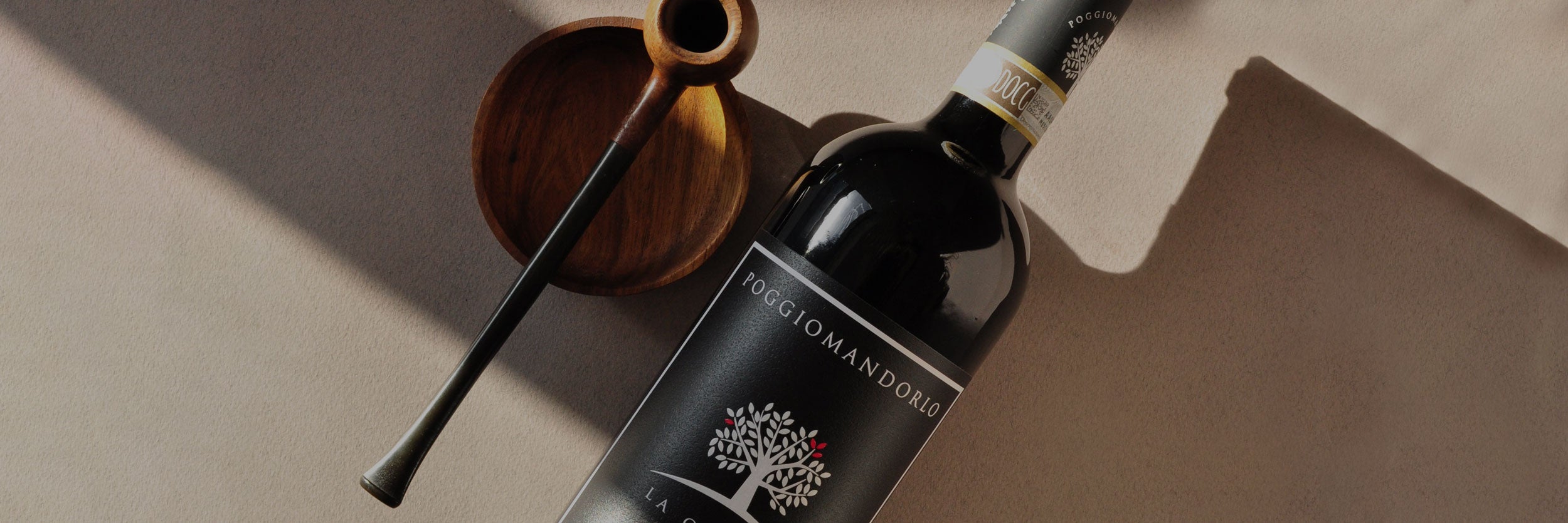 Styled close-up of Poggio Mandorlo La Querce Sangiovese beside a vintage pipe — a minimal-intervention Tuscan red wine evoking depth and tradition