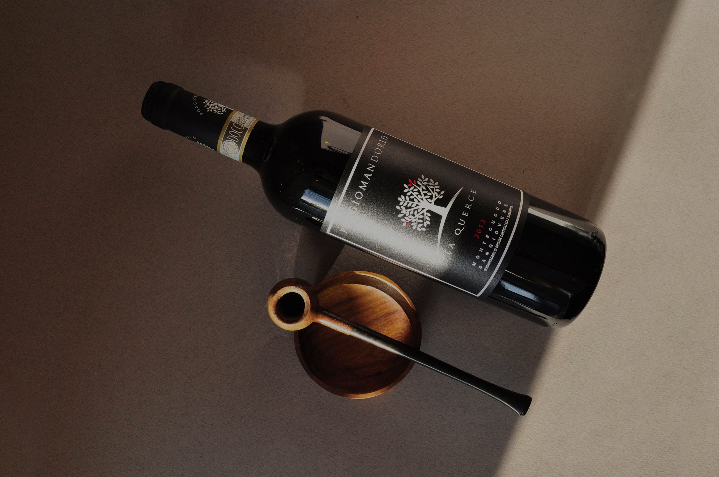 Poggio Mandorlo La Querce Sangiovese styled beside a pipe — a bold and refined organic red wine from Montecucco, Tuscany, rich in heritage and character